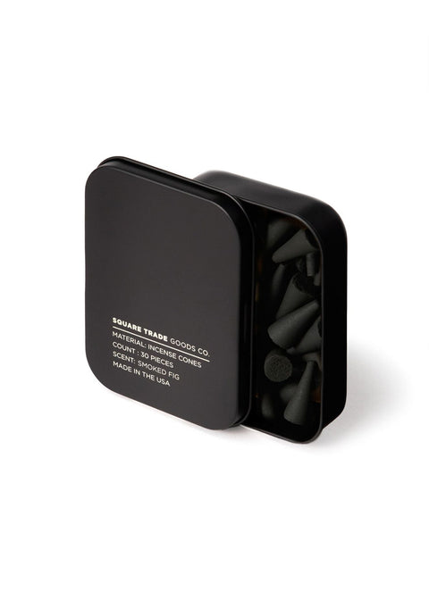 A black tin container with incense cones visible inside. The lid is labeled with the product name 'Hinoki' and mentions the scent notes and burn time.